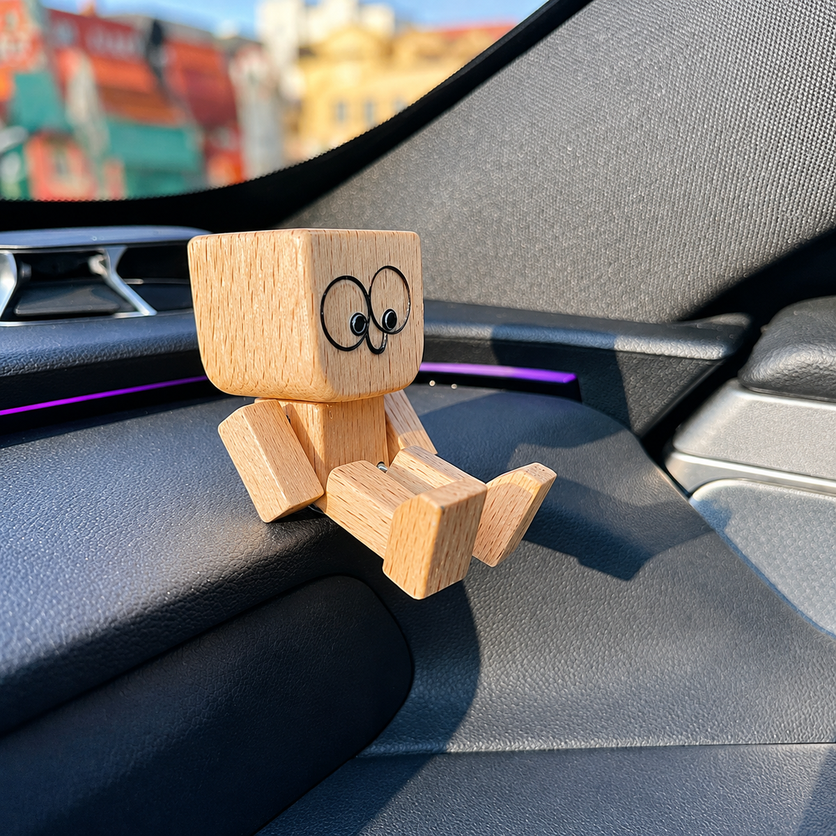 Side view of the wooden figure on a car dashboard in sunlight, showing its cube head and jointed limbs. 2