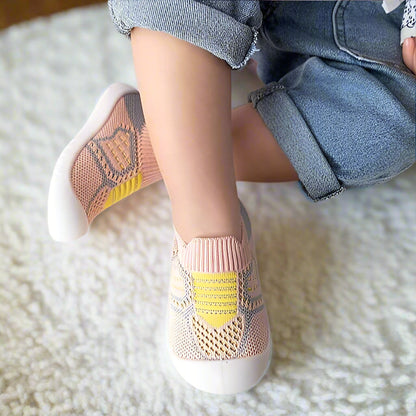 Child's crossed legs show pink knit shoes with yellow panels and open mesh weave, resting on a soft white rug. 13