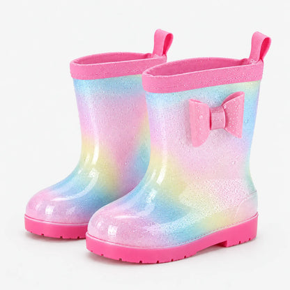 Pair of glittery pastel rainbow wellies with a pink bow, pink rim and pull tabs, dotted with water droplets. 7