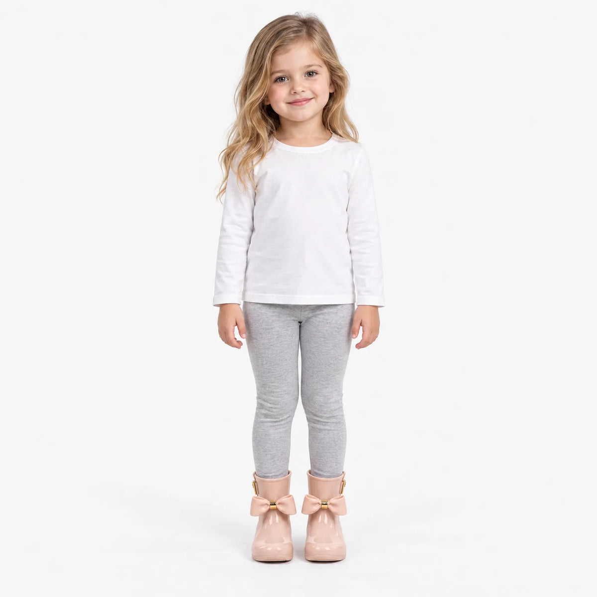 Smiling girl in a white top and grey leggings wearing pink bow wellies, full-length shot on white background. 4