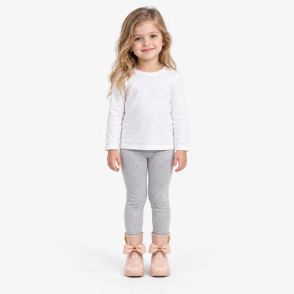 Smiling girl in a white top and grey leggings wearing pink bow wellies, full-length shot on white background. 4