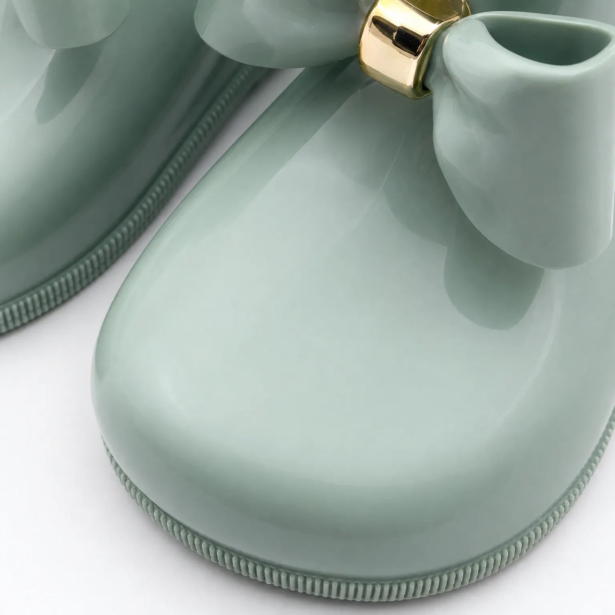 Close-up of the rounded toe, ridged sole edge and gold-banded bow on a glossy sage green welly. 6