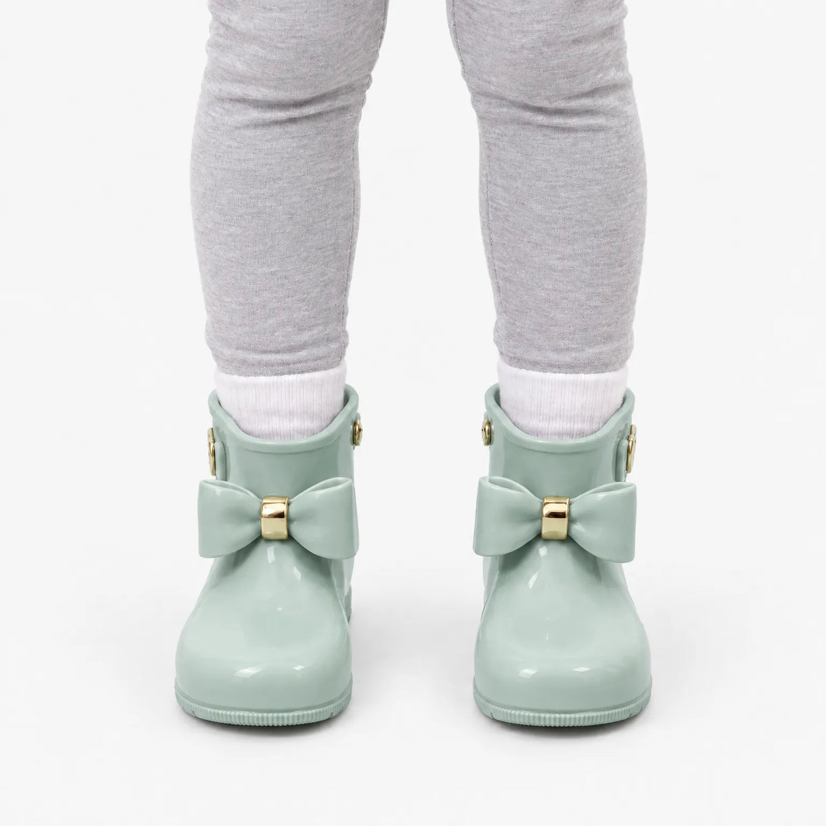 Front view of a child wearing sage green bow wellies with white socks and grey leggings. 8