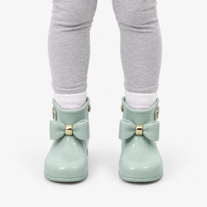 Front view of a child wearing sage green bow wellies with white socks and grey leggings. 8