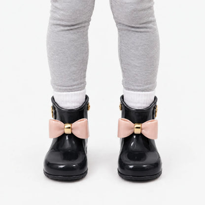 Front view of a child wearing black glossy wellies with pink bows, white socks and grey leggings. 9