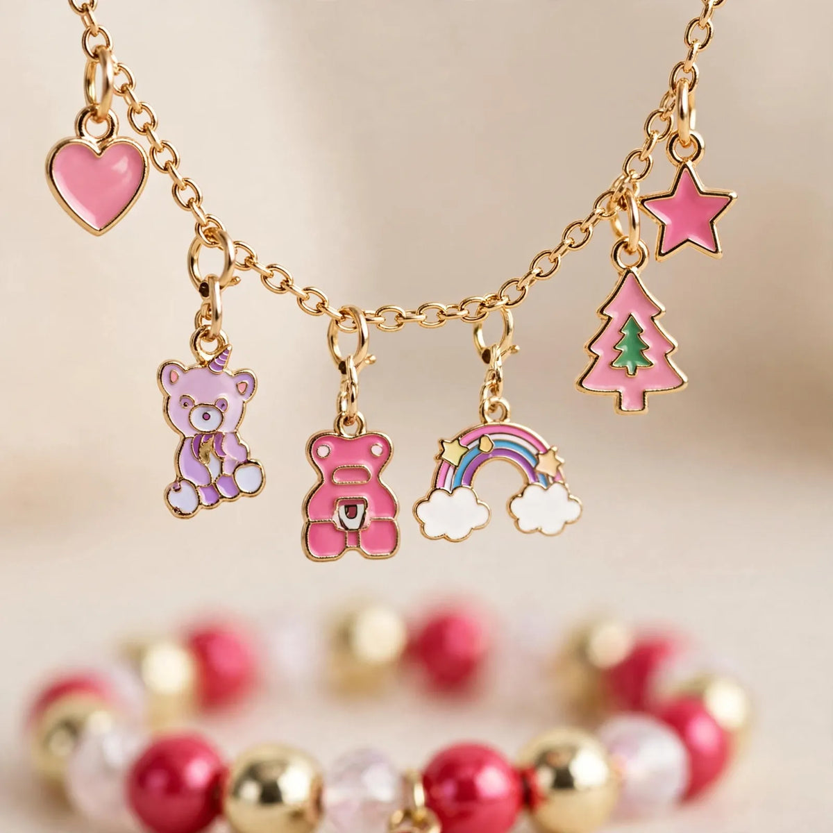 Close-up of a gold chain hung with pink enamel charms: heart, bears, rainbow, tree and star 3