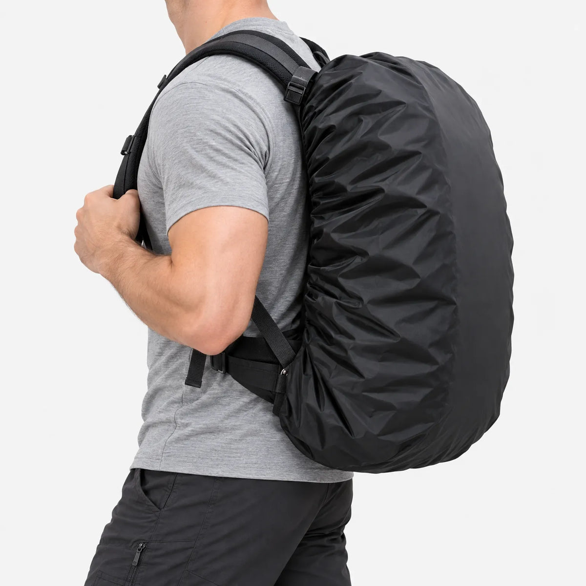 Side view of a man in a grey t-shirt and dark trousers carrying a backpack fitted with a black cover against a white background. 4