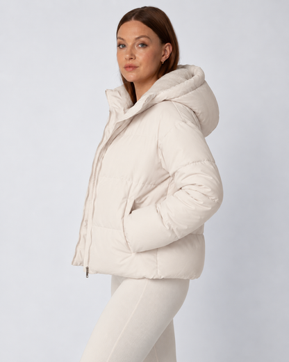 Side view of the cream puffer jacket with hood up, model's hand in the pocket 3