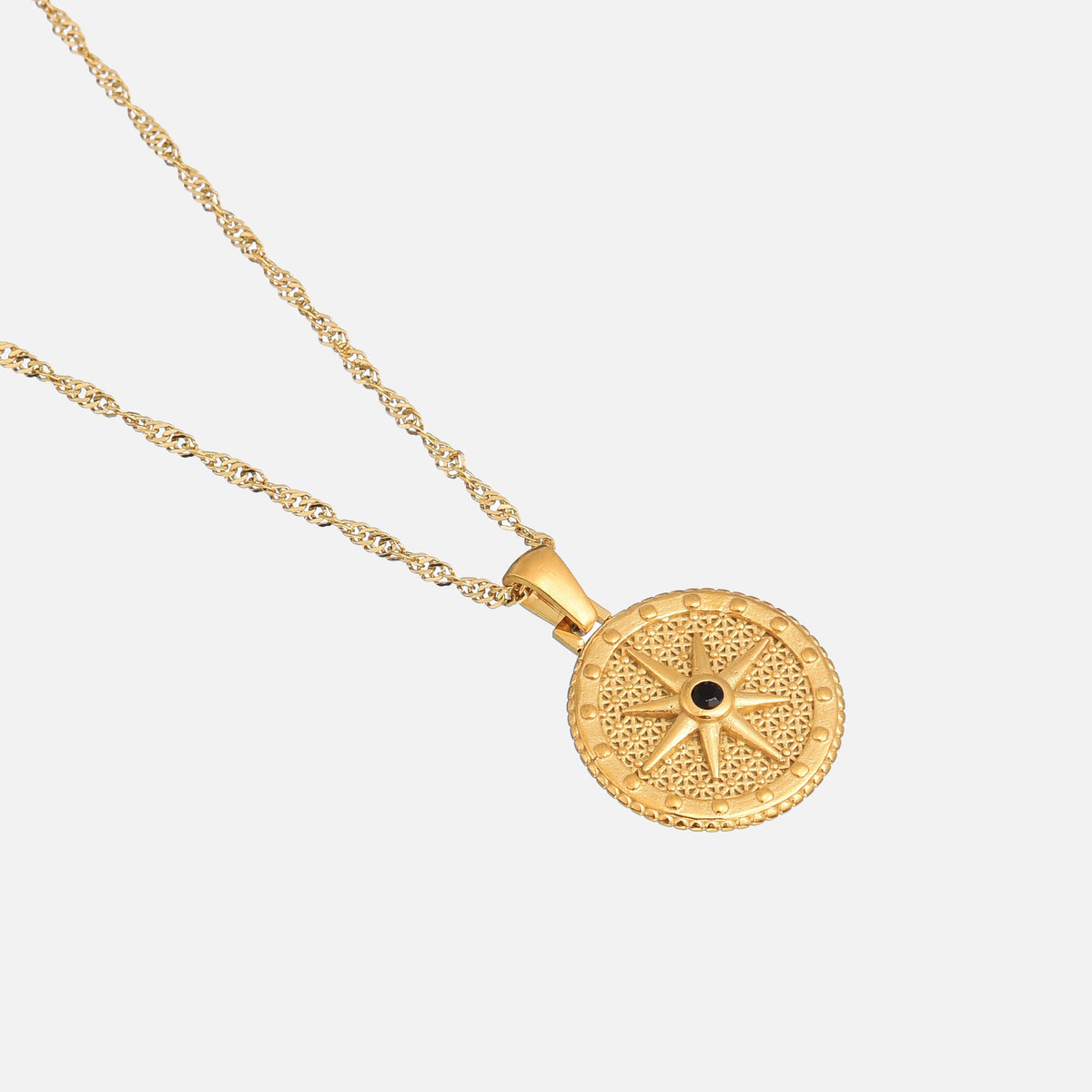 Angled view of the round gold star pendant and its twisted chain, lying flat against a pale background. 2