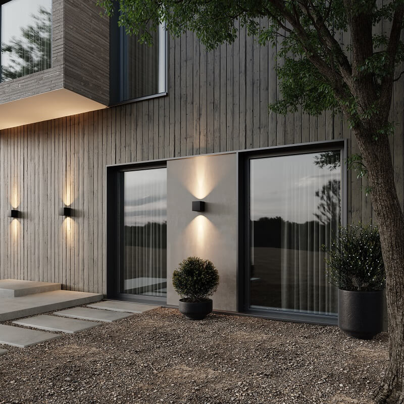 Black cube wall lamps lighting up and down on a timber-clad house exterior at dusk, near large windows and potted plants. 3
