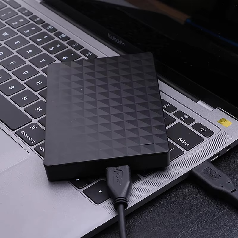 Black textured drive resting on a laptop keyboard, connected by a USB cable 3