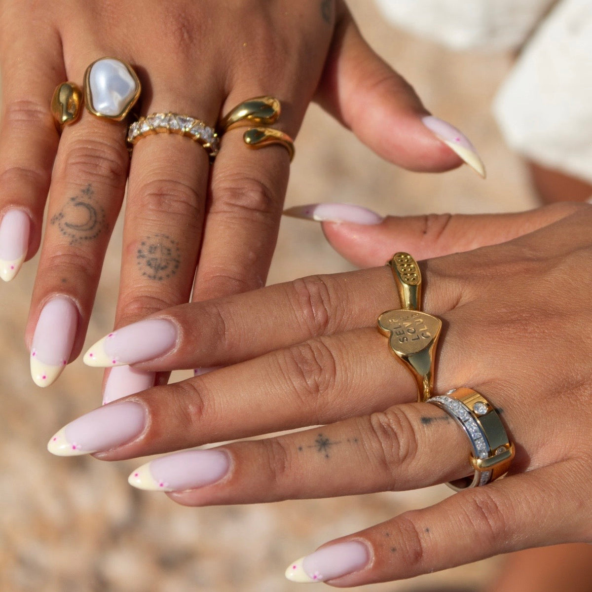 Ring worn on a finger of a manicured hand, styled with gold signet rings and a pearl ring 4