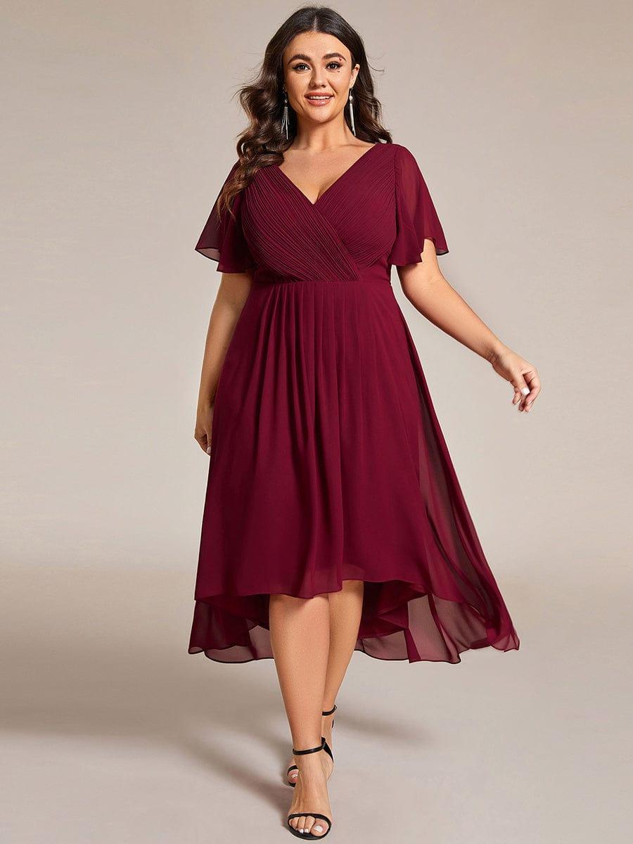 Plus-size model in the burgundy high-low dress with flutter sleeves, wearing long drop earrings and black heels. 49
