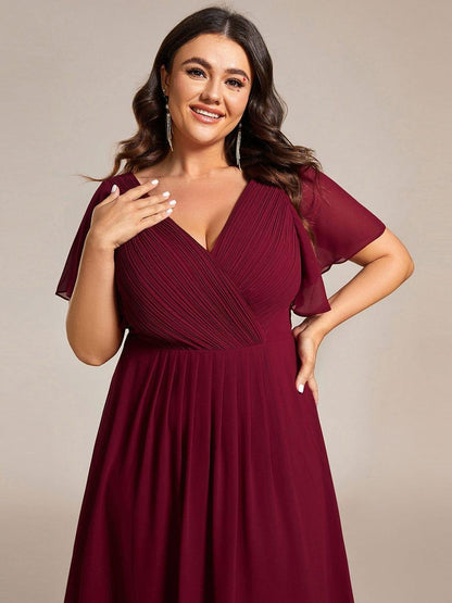 Close-up of the burgundy pleated V-neck bodice and flutter sleeves on a plus-size model with one hand at her chest. 51