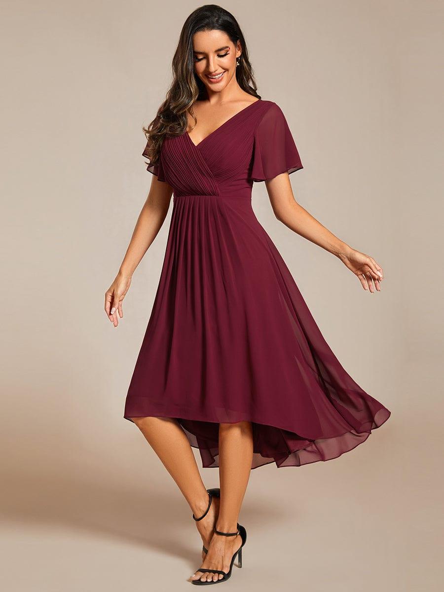 Model in the burgundy high-low chiffon dress with black strappy heels, looking down and smiling as the skirt moves. 47