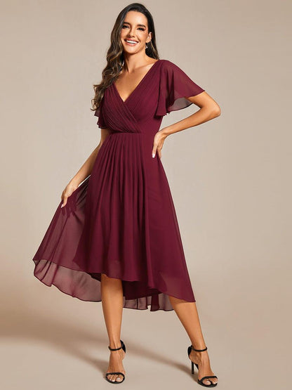 Burgundy chiffon dress with pleated V-neck, model smiling with one hand on hip and lifting the sheer skirt edge. 48