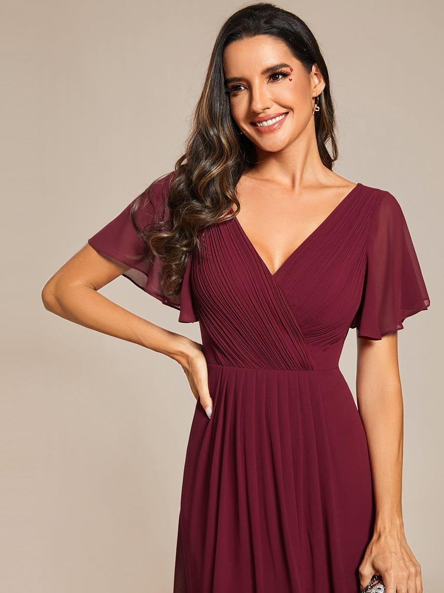 Close-up of the burgundy dress's pleated crossover V-neck and sheer flutter sleeves on a smiling model. 46