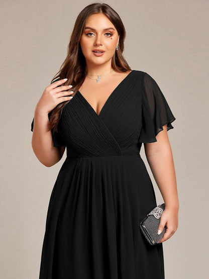 Close-up of the black dress on a plus-size model, showing the pleated wrap bodice and sheer sleeves, holding a sparkly clutch. 28