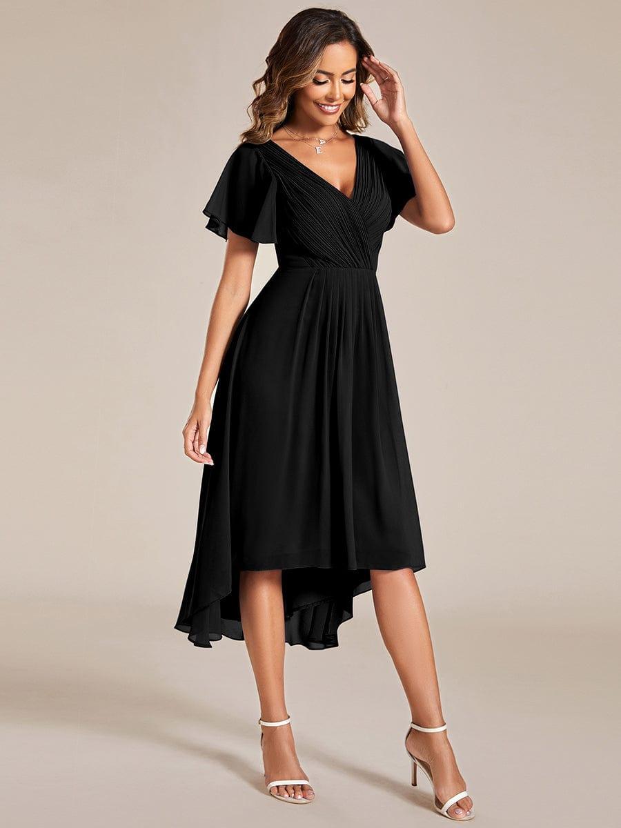 Three-quarter view of the black dress on a smiling model, showing the pleated waist and high-low hem. 25