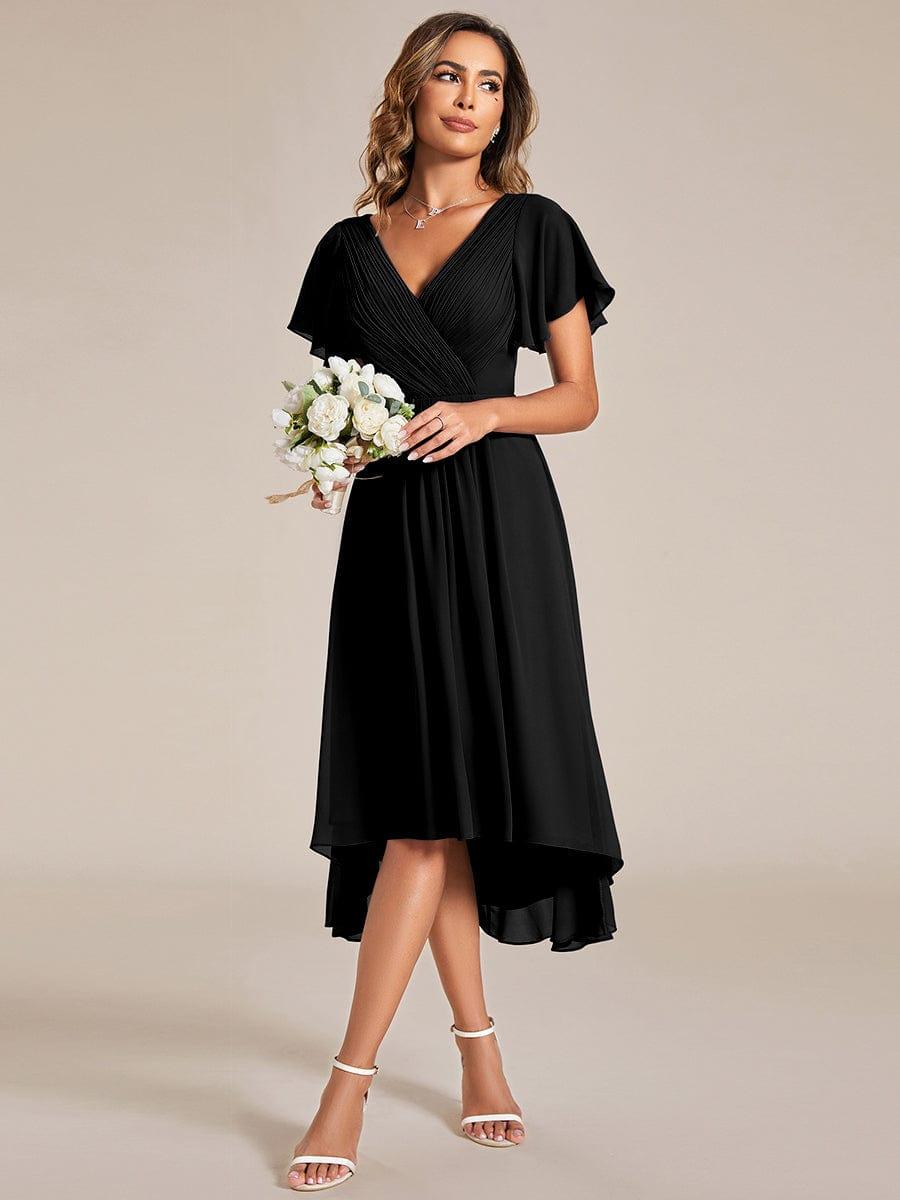 Model in the black dress holding a small bouquet of white flowers, glancing to the side in white heels. 24