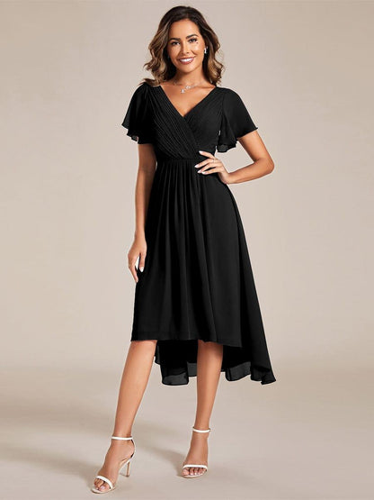 Model in a black chiffon dress with pleated wrap bodice and flutter sleeves, one hand on hip, front view with white heels. 21