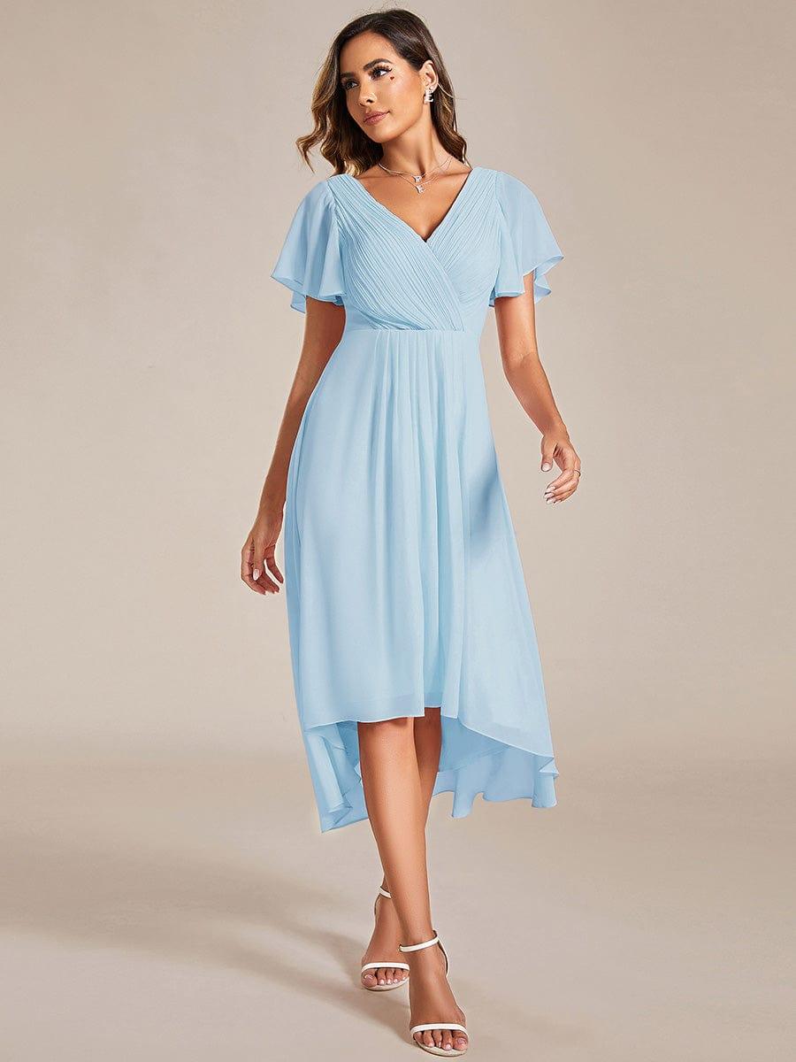 Model in a light blue high-low chiffon dress with pleated V-neck bodice and flutter sleeves, walking towards the camera in white heels. 84
