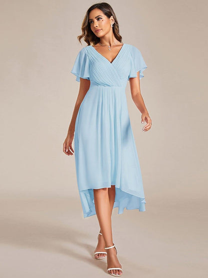 Model in a light blue high-low chiffon dress with pleated V-neck bodice and flutter sleeves, walking towards the camera in white heels. 84