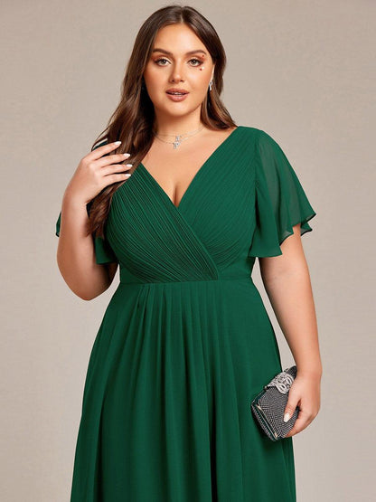Close-up of the dark green dress's pleated wrap bodice and sheer sleeves, with the model holding a sparkly clutch. 38