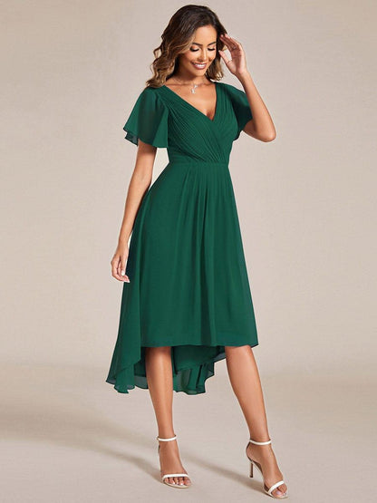 Emerald green dress in a side-on pose, one hand raised to the hair, showing the pleated waist and hem. 14