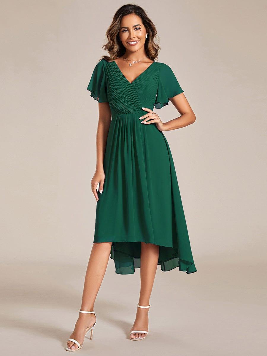 Front view of the emerald green dress on a model with hand on hip, pleated bodice and high-low skirt. 10