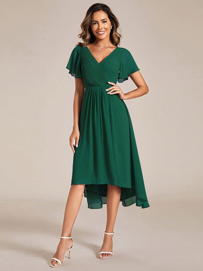 Front view of the emerald green dress on a model with hand on hip, pleated bodice and high-low skirt. 10