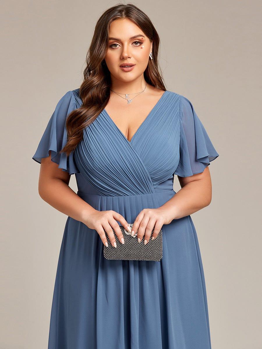 Close-up of the pleated wrap V-neck bodice and flutter sleeves in dusty blue, with the model holding a sparkly clutch. 43