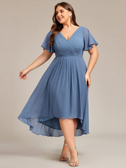 Plus-size model in a dusty blue chiffon dress with pleated V-neck, flutter sleeves and high-low hem, smiling in silver sandals. 41