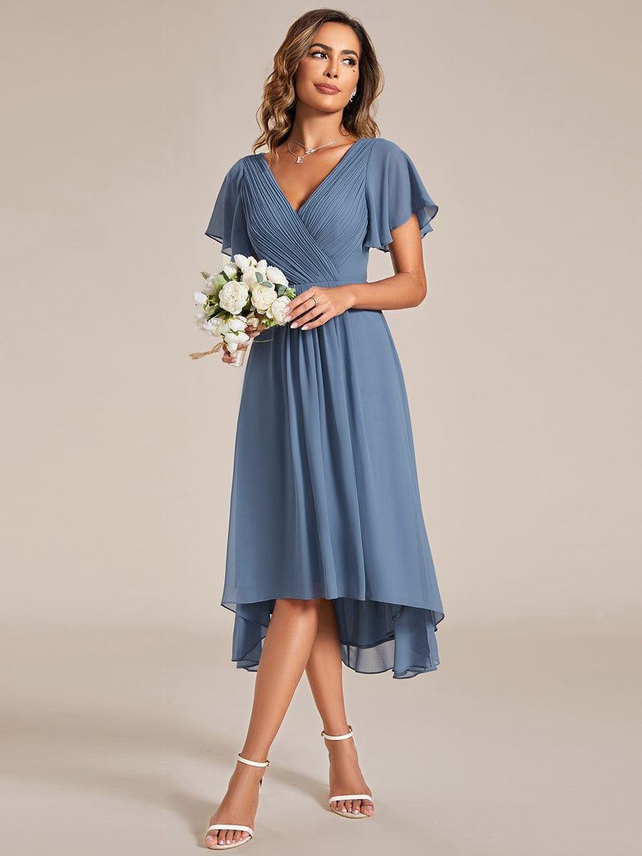 Dusty blue dress worn by a model holding a bouquet of white flowers, showing the high-low hemline. 8