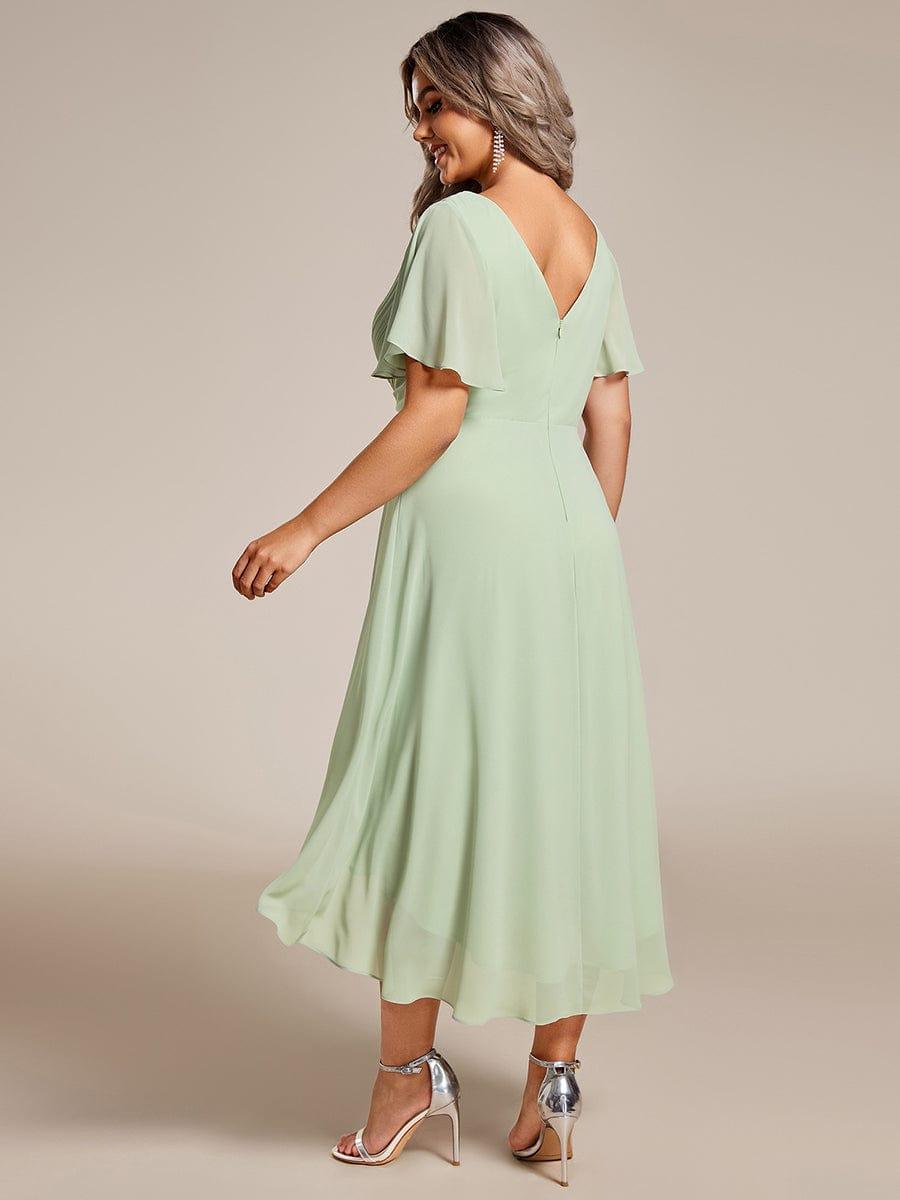 Back view of the sage green high-low chiffon dress on a plus-size model, showing the V-shaped back, zip and flowing hem. 82