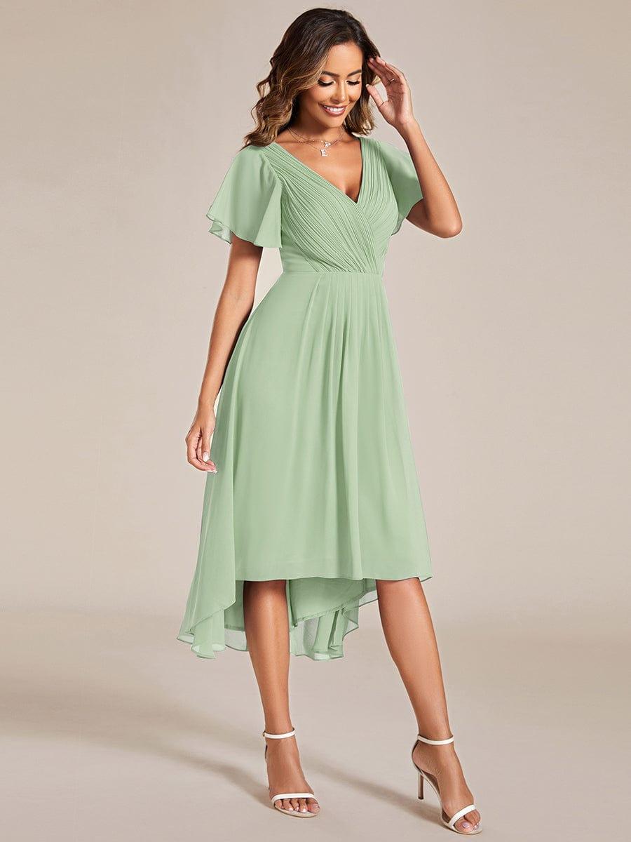 Sage green high-low chiffon dress worn by a model touching her hair, shown from a three-quarter front angle. 80