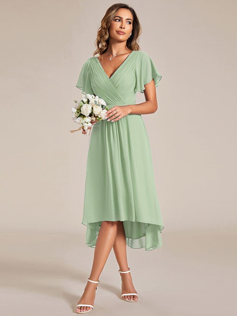 Model in the sage green dress holding a bouquet of white roses, showing the high-low hem and white sandals. 79