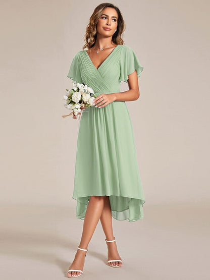 Model in the sage green dress holding a bouquet of white roses, showing the high-low hem and white sandals. 79