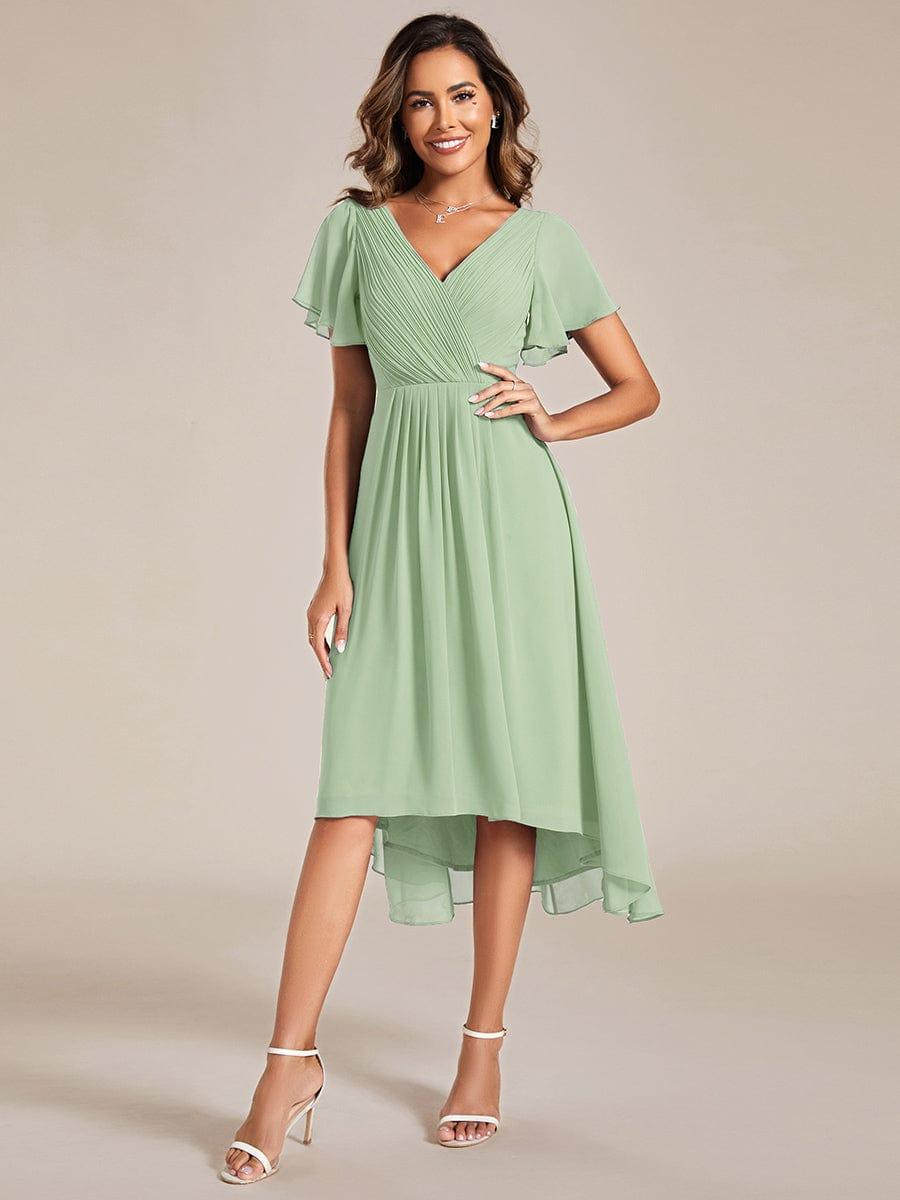 Sage green chiffon version of the dress with pleated V-neck, flutter sleeves and high-low hem, model with hand on hip. 76