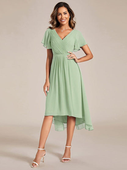Sage green chiffon version of the dress with pleated V-neck, flutter sleeves and high-low hem, model with hand on hip. 76