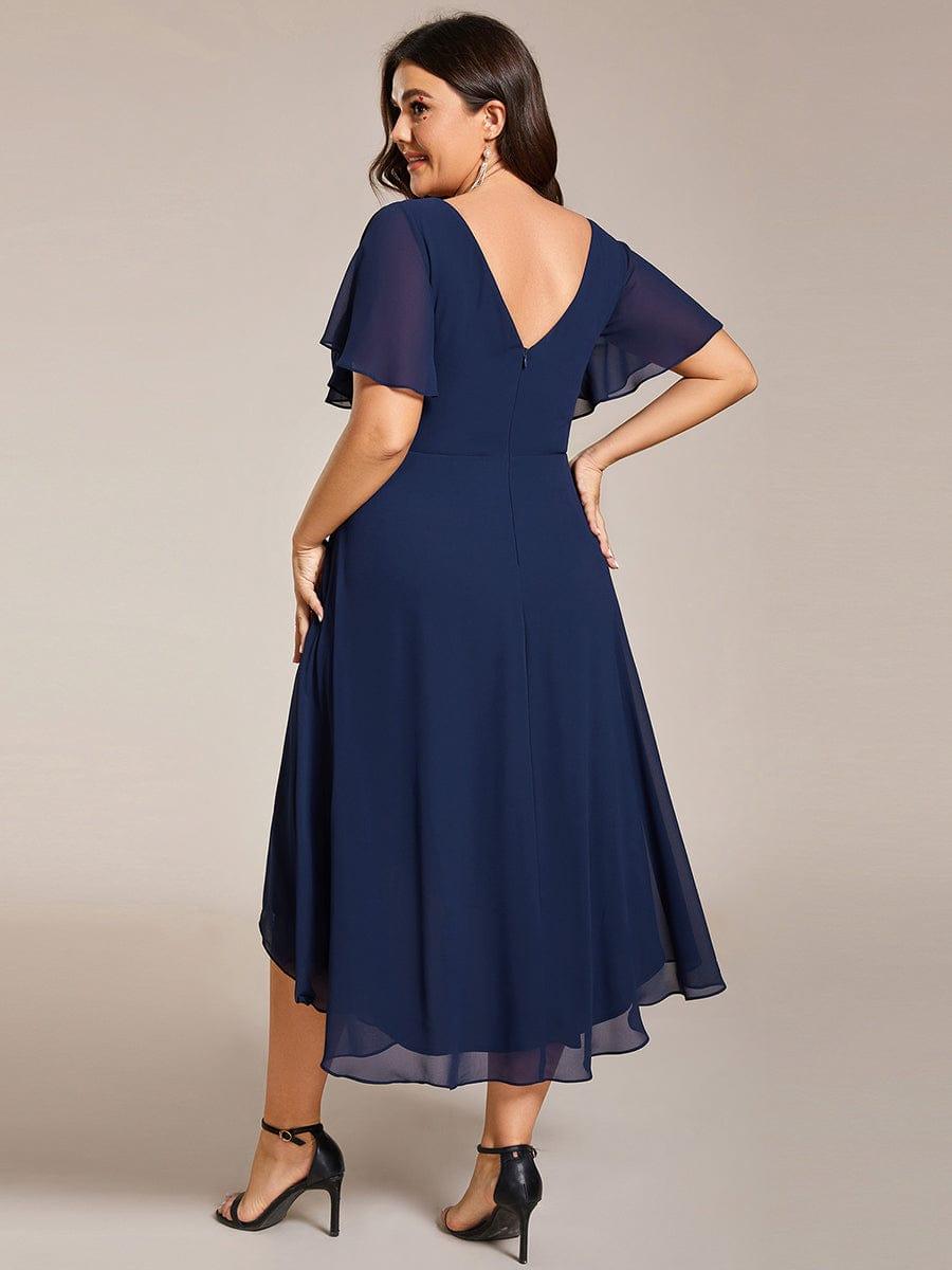 Back view of the navy dress on a plus-size model, showing the V-shaped back, zip and layered chiffon hem. 56
