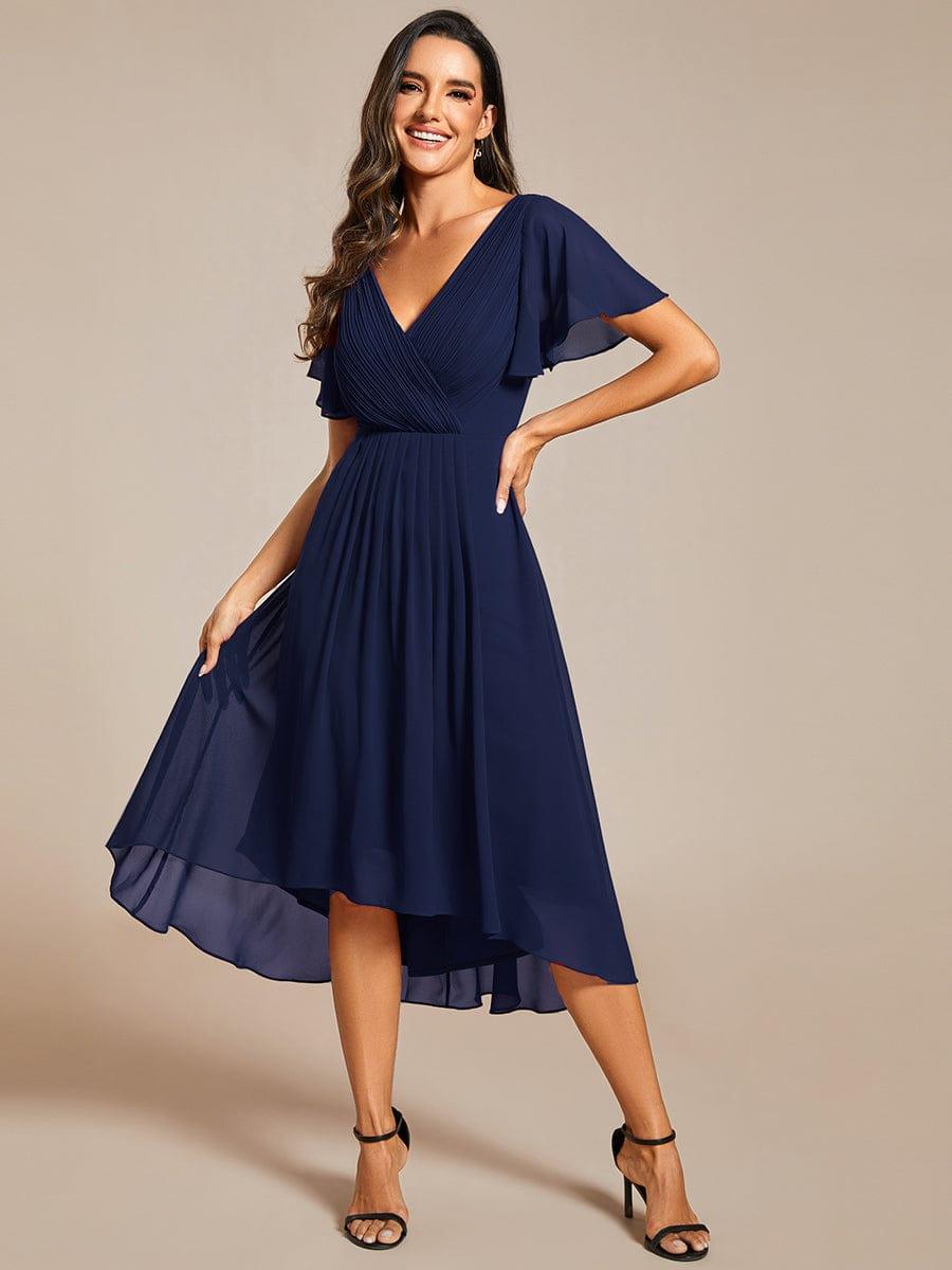 Navy chiffon dress with high-low hem, model smiling with hand on hip and lifting the sheer skirt. 54