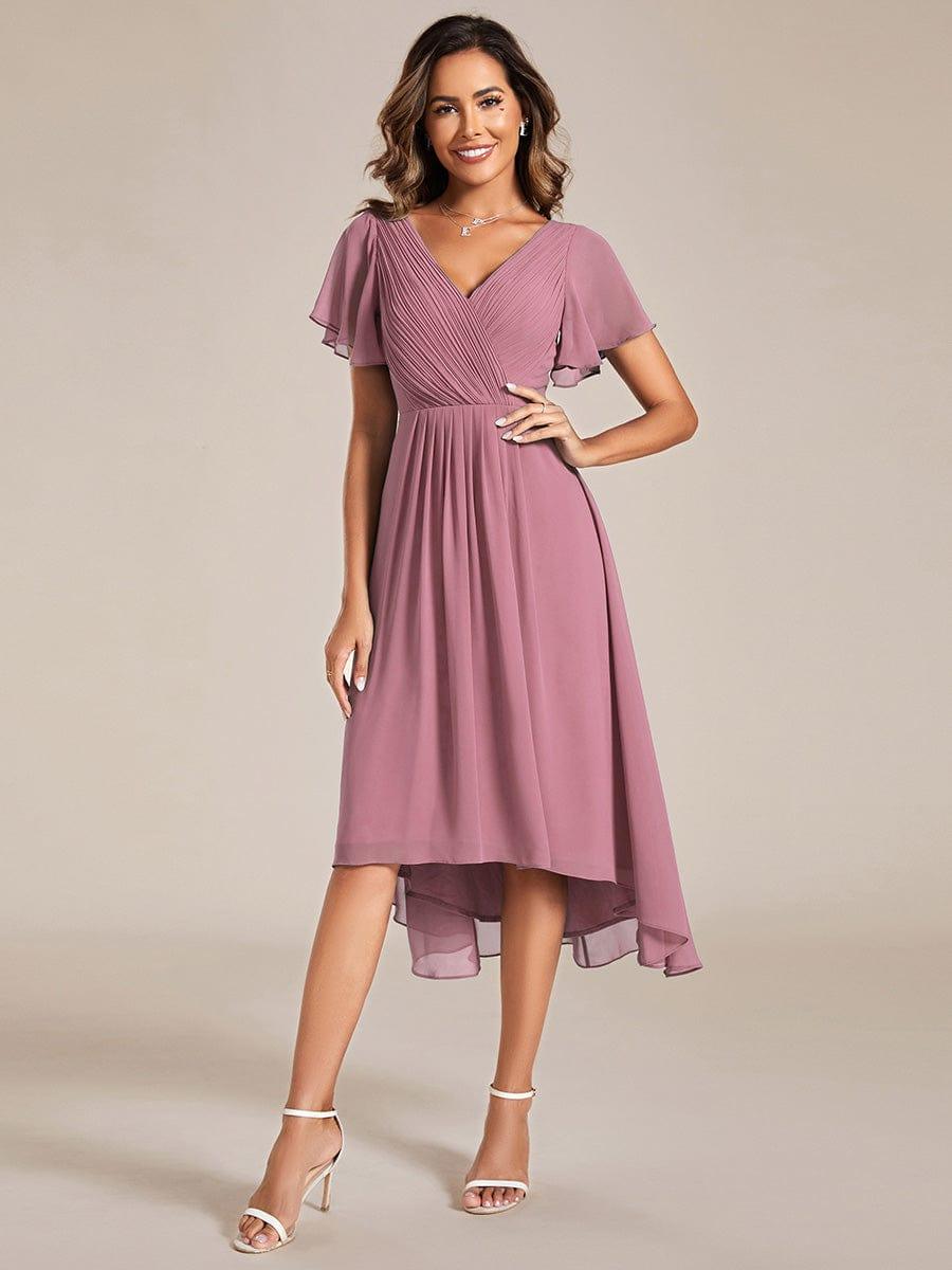 Model in the mauve-pink high-low chiffon dress with pleated V-neck and flutter sleeves, wearing white heels, hand on hip. 58
