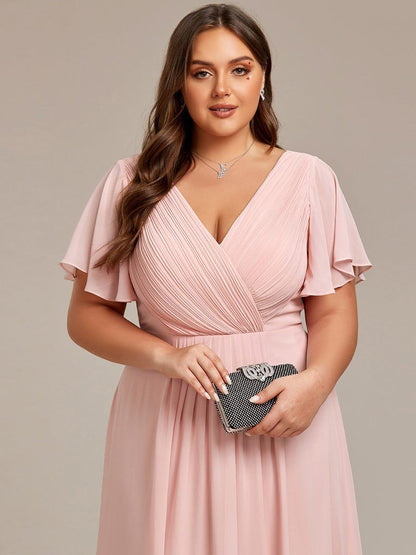 Close-up of the pink dress's pleated wrap bodice and flutter sleeves, with the model holding a studded clutch. 33