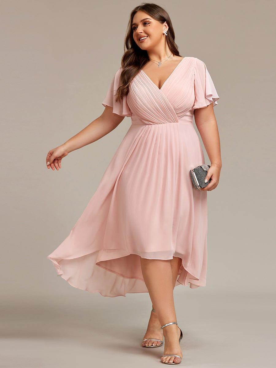 Plus-size model in the dress in soft pink, walking with one arm out and holding a clutch, with silver heels. 31