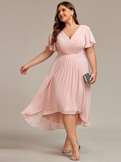 Plus-size model in the dress in soft pink, walking with one arm out and holding a clutch, with silver heels. 31