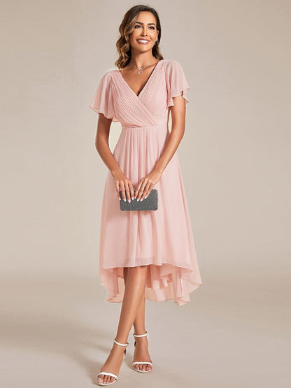 Front view of the pink chiffon dress on a model holding a small black clutch with both hands. 15