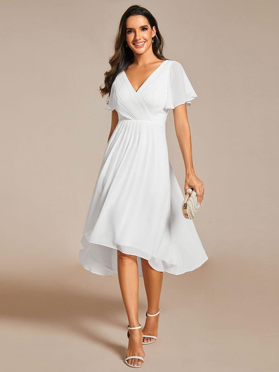 White chiffon version of the dress with pleated V-neck and flutter sleeves, worn with a pearl clutch and white heels. 68