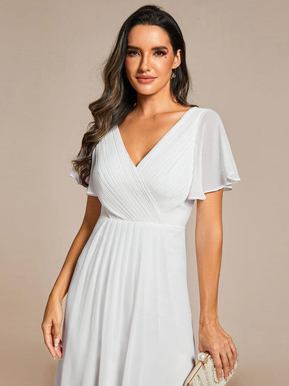 Close-up of the white dress's pleated wrap bodice and sheer flutter sleeves, model holding a pearl-embellished clutch. 70