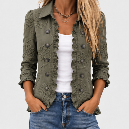 Close-up of the olive green jacket worn open over a white vest top and jeans, showing ruffled edges and floral embroidery. 1